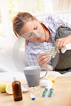 Woman having flu taking medicines in bed