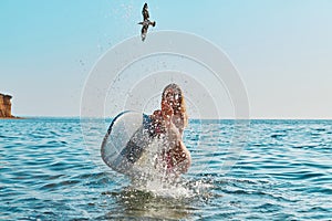 Woman having fun in ocean, spray with water. Bird flying in blue sky. Holiday trip, surfing sport and summer time idea