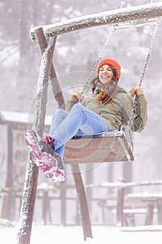 Woman having fun swinging in the playground on snowy winter day outdoors
