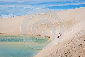 Woman having a good time, rolling down a huge sand dune in a amazing scenario, natural pool lagoon in the bottom. North of Brasil,