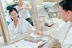 Woman having hair dried reading magazine