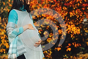 Woman having happy pregnancy time. Pregnant woman's belly over autumn background