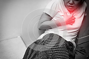 Woman having heart attack, chest pain, or heartburn from GERD, isolated in white background with red spot on chest. Black and whit
