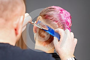 Woman having a new haircut. Male hairstylist cutting pink short hair with scissors in a hair salon.