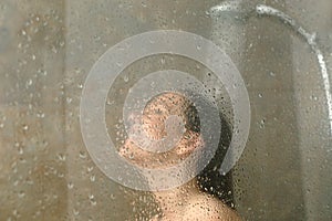 Woman having shower behind glass on a bathroom