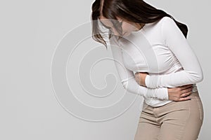 Woman having a stomachache, menstruation pain or cramps, isolated on grey background