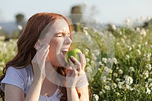 Woman having toothache while eating a green apple