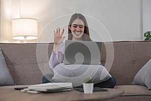 Woman having video call on her laptop at home. Smiling girl smile to family or friends