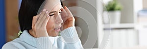 Woman with headache and photophobia looks out window photo