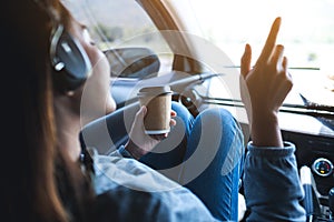 A woman with headphone enjoy listening to music and drinking coffee in the car