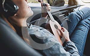A woman with headphone playing Ukulele in the car