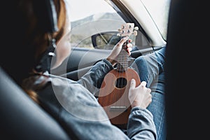 A woman with headphone playing Ukulele in the car