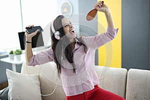 Woman in headphones on couch holds smartphone in her hands and pretends to sing