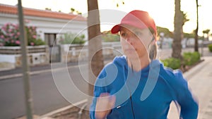 Woman with headphones in ears runs down the street along the palm avenue at sunset. Healthy active lifestyle