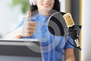Woman in headphones in front of microphone in studio showing thumb up sign