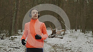 Woman in headphones jogging in park. Motivated female athlete running and hard training in the morning in winter forest. Professio