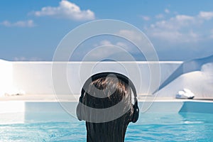 Woman in the headphones listening to the  music bathing in a pool