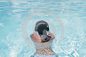 Woman in the headphones listening to the  music bathing in a pool