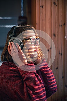 A woman with headphones looks through the blinds at the early morning sunlight.