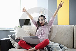 Woman in headphones sit on sofa in room and rejoice.