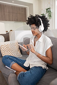 Woman in headphones sitting on sofa and using phone