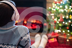 Woman in headphones sitting and warming at winter evening near fireplace flame and  christmas tree.