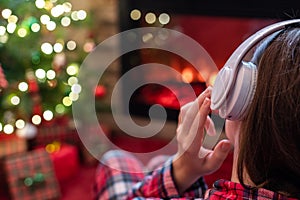 Woman in headphones sitting and warming at winter evening near fireplace flame and  christmas tree.