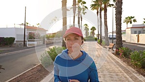 Woman with headphones and smartphone runs down the street along the palm avenue at sunset. Healthy active lifestyle