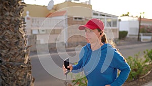 Woman with headphones and smartphone runs down the street along the palm avenue at sunset. Healthy active lifestyle