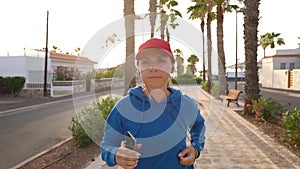 Woman with headphones and smartphone runs down the street along the palm avenue at sunset. Healthy active lifestyle