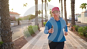 Woman with headphones and smartphone runs down the street along the palm avenue at sunset. Healthy active lifestyle