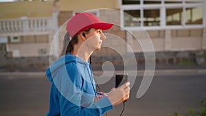 Woman with headphones and smartphone runs down the street along the palm avenue at sunset. Healthy active lifestyle