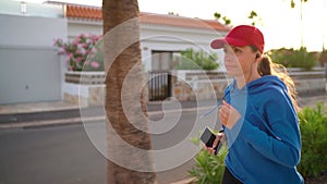 Woman with headphones and smartphone runs down the street along the palm avenue at sunset. Healthy active lifestyle