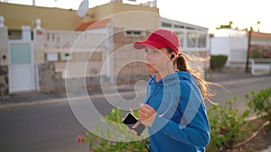 Woman with headphones and smartphone runs down the street along the palm avenue at sunset. Healthy active lifestyle