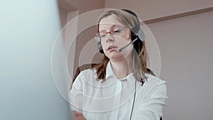 Woman in headphones speaking to a client, call center worker, work from home.