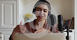 Woman in headphones talking into microphone records podcast on computer