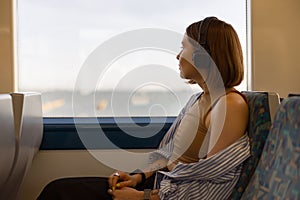 Woman in headphones while traveling in public transport and looking view outside the window