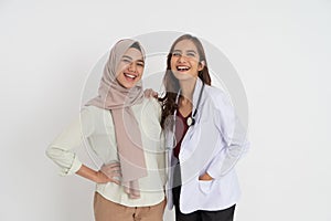 woman in headscarf and beautiful female doctor laughing together looking at camera embracing pose