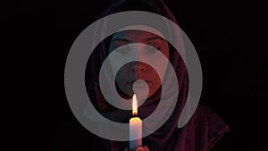 Woman in a headscarf with a burning candle in hands praying to god in darkness