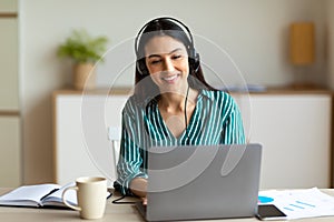 Woman In Headset Making Video Call Sitting At Laptop Indoor