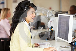 Woman With Headset Working At Desk In Busy Creative Office