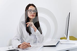 Woman healthcare worker doing some paperwork and using computer while working at doctor`s office.