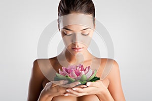 Woman with healthy clean hydrated skin and natural makeup holds a lotus flower