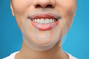 Woman with healthy teeth and beautiful smile on blue background, closeup. Cosmetic dentistry