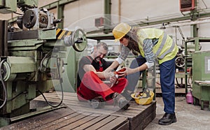 Woman is helping her colleague after accident in factory. First aid support on workplace concept.