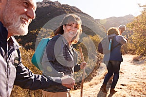 Woman Helping Man On Trail As Group Of Senior Friends Go Hiking In Countryside Together