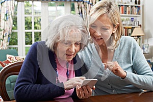 Woman Helping Senior Neighbor To Use Mobile Phone