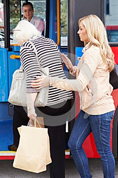 Woman Helping Senior Woman To Board Bus