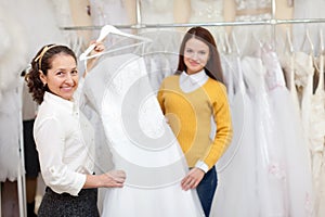 Woman helps the bride in choosing bridal gown