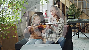 A woman helps a child pick up a violin and teaches how to play